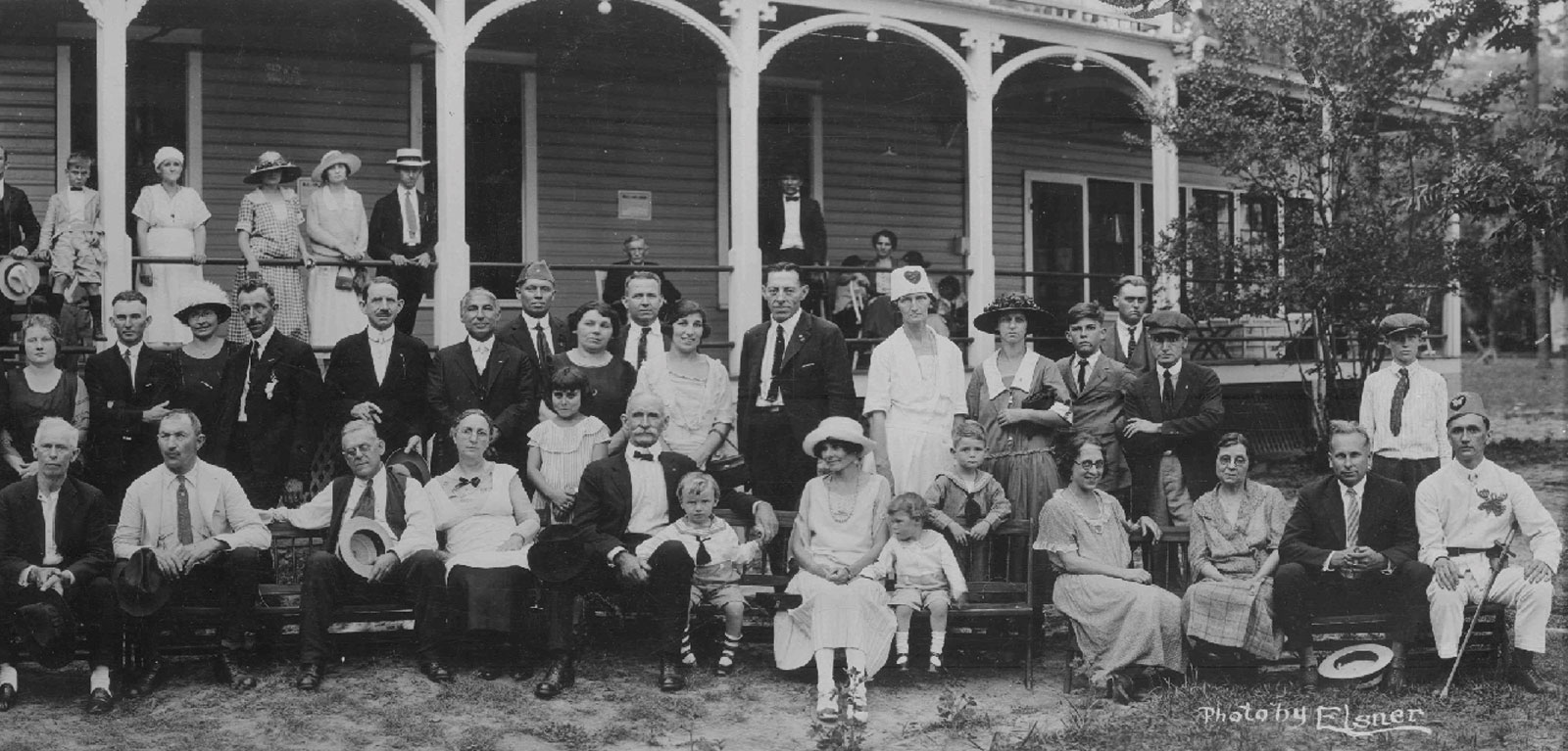 Residents of the early Moosehaven, along with family members, pose on the front porch of Bradon Hall. Black and white photo shows men, women, and children in 1920s attire.