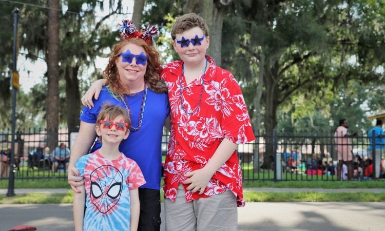 A mom, teenage son, and younger son dressed in 4th of July outfits and glasses stand outside Moosehaven awaiting the fireworks.