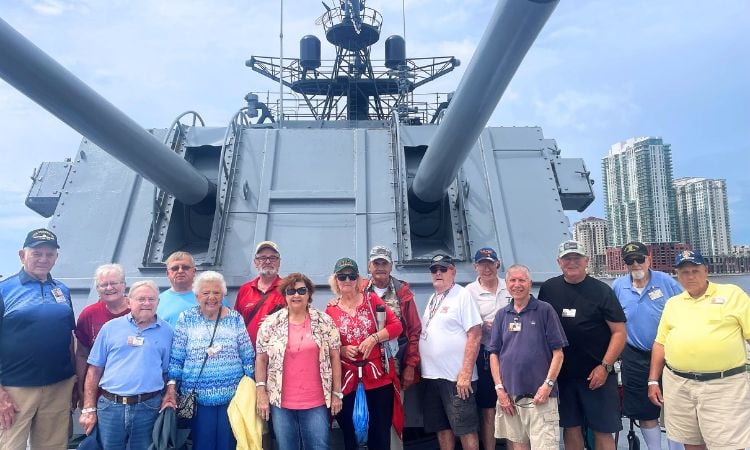 A group of veterans stands on deck aboard the USS Orleck.
